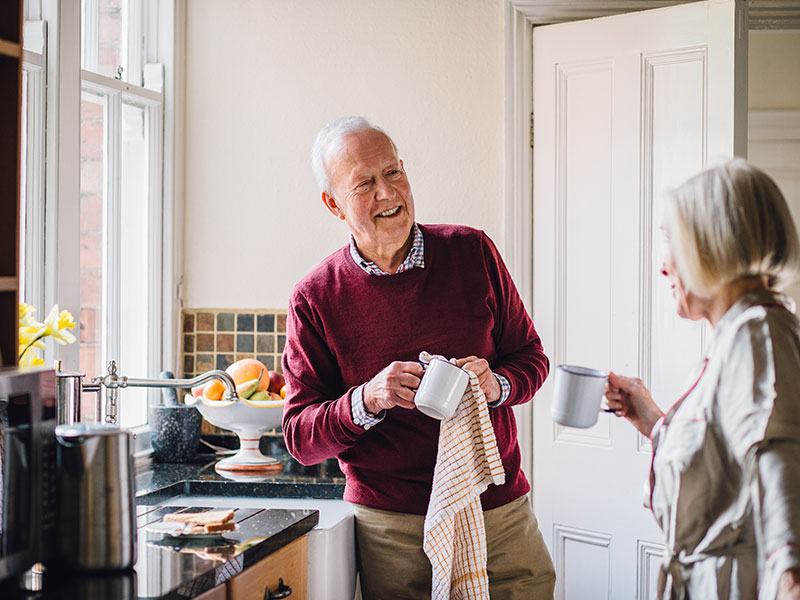 Elderly man and woman enjoying a moment in the kitchen while drinking coffee and eating toast