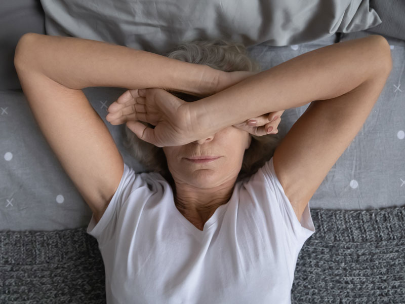 Elderly woman suffering from chronic fatigue is laying on a bed, exhausted and frustrated with her lack of energy.