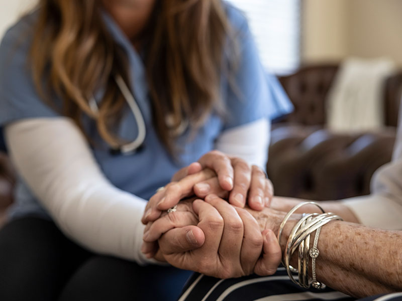 Young medical professional wearing a stethoscope holding the hands of an elderly person, giving advice on how to improve quality of life.