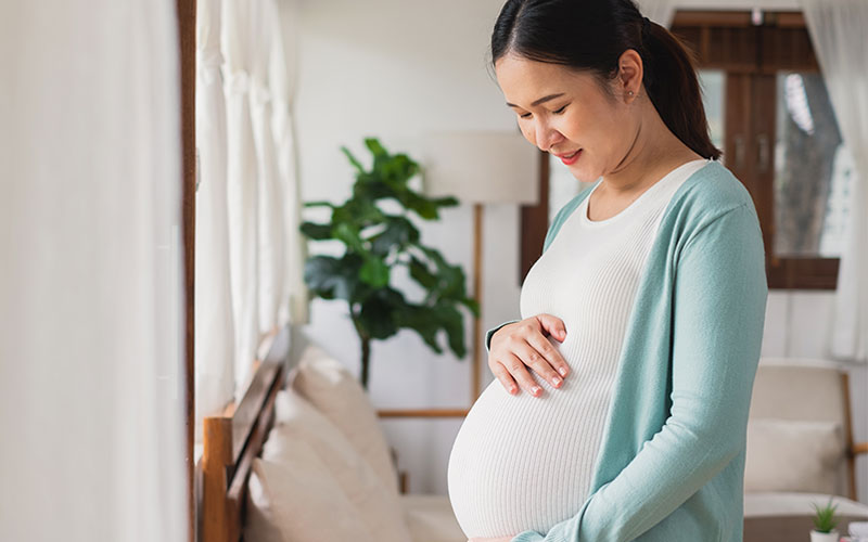 Pregnant Asian woman holding her stomach while smiling