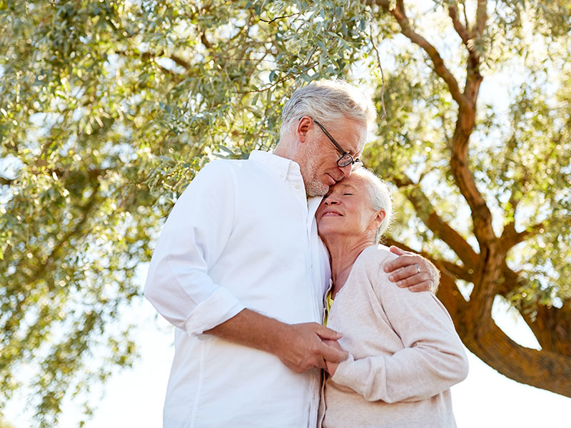 Middle-aged couple in light clothes hugging as they're enjoying old age and their retirement.
