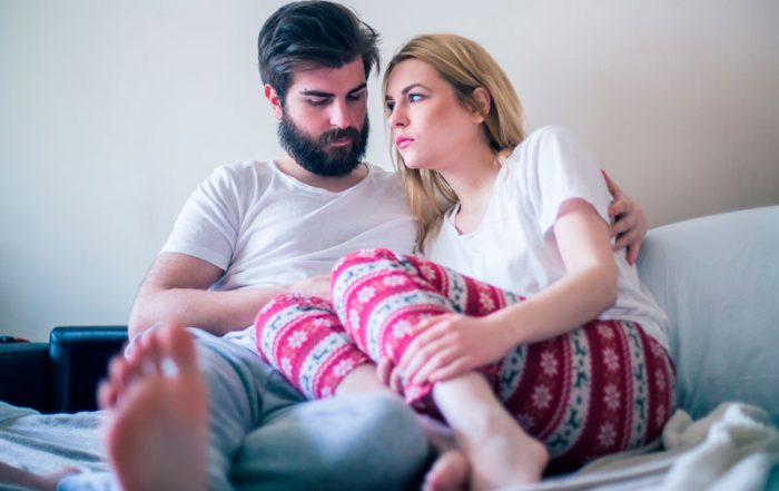 Couple sitting on bed looking sad and discouraged due to problems with infertility. The man is comforting the woman.